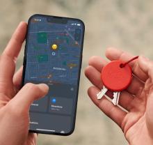Image of hands with one holding keys with a red circular keyring on them, and the other hand holding a phone with a map image on it showing the location of the red circular keyring. 