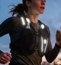 Person running wearing a black running vest with reflective panels and a water bottle in the front pocket. 