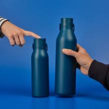 Image of two dark blue reusable water bottles against a mid-blue background. The left bottle is smaller and has a hand pointing to its lid, and the right bottle is larger with a hand holding it. 