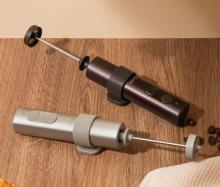 Image of two handheld milk frothers placed on a wooden surface. One in a metallic brown colourway, and the other in a metallic champagne colourway. 