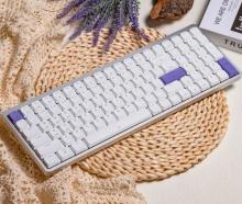 Image of silver keyboard with white keys, and some purple keys. The keyboard is on a woven circle material mat. 