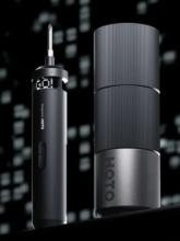 Image of black electric screwdriver with a digital display at the top saying 'Go!', next to a black cylinder screwdriver case. The screwdriver and case are against a black and white blurred pixelated background. 