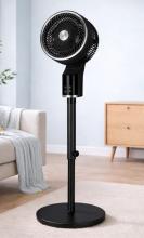 Image of black pedestal fan with circular base, in a living room setting. 