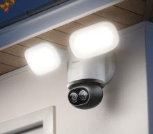 Image of modern outdoor security camera with two bright LED floodlights mounted under a roof eave. 
