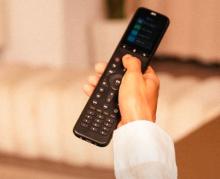 Image of hand with white sleeve, holding a black remote control. 